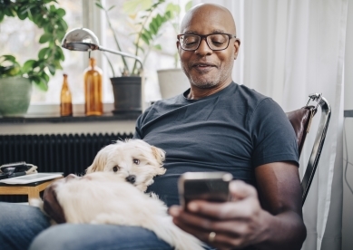 gentlemen with a white dog on his lap while he is look at his cell phone with his left hand